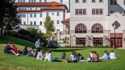 students attending class outside, sitting on lawn